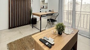 A modern living room with a wooden coffee table, a TV mounted on a wooden panel, a dining area with a table and chairs, and a large window with curtains. - Athens Studio in the sky...❗️❗️❗️ perfect for couples❤️️ (Kallithea)