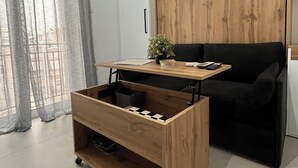 A modern living room with a wooden cabinet, a black sofa, a small wooden table with a plant, and a storage unit with wheels. - Athens Studio in the sky...❗️❗️❗️ perfect for couples❤️️ (Kallithea)