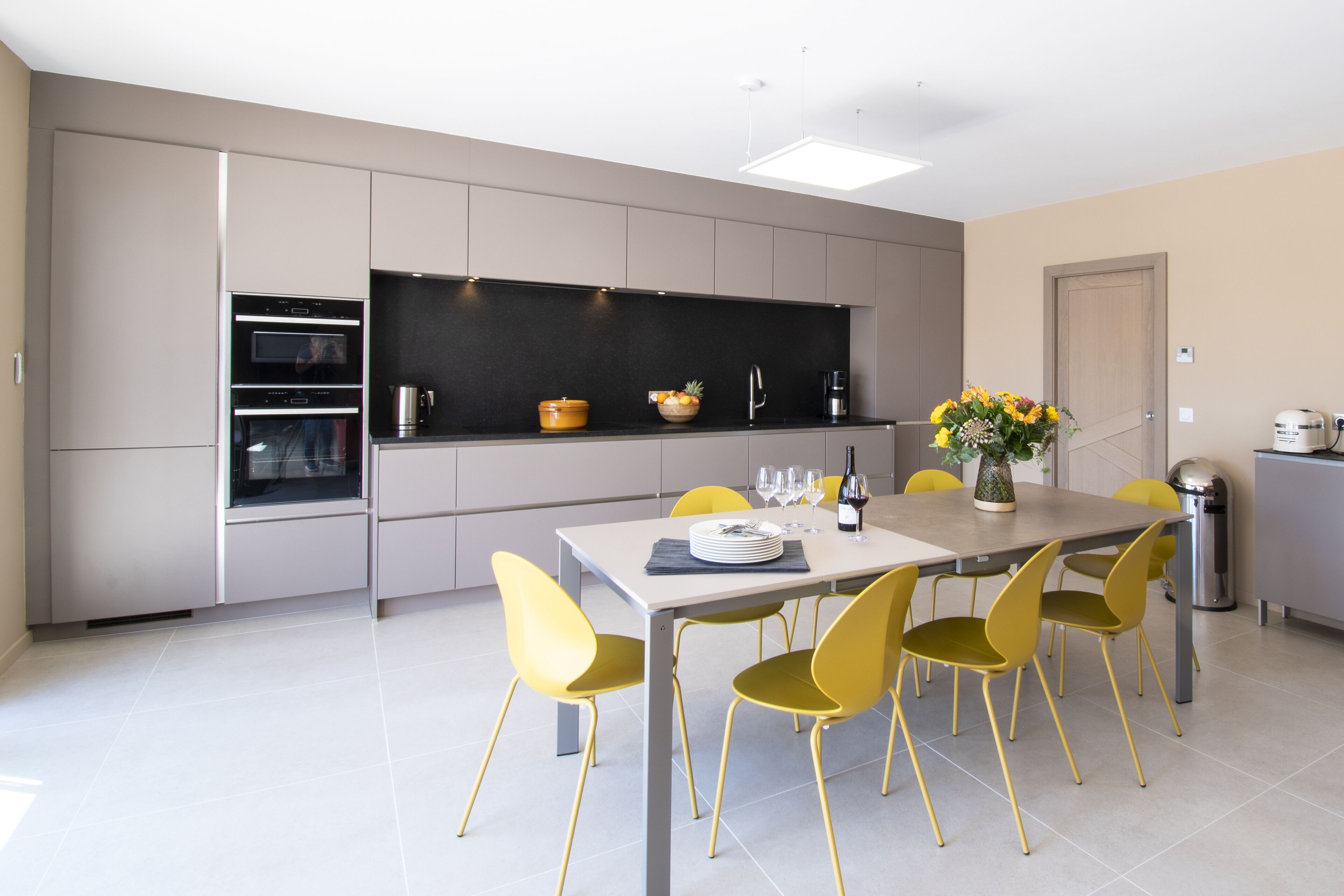 Une cuisine moderne dotée d’appareils électroménagers intégrés, une table à manger avec des chaises jaunes et un vase de fleurs posé sur la table.