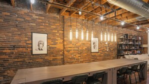 Un long comptoir en bois avec des chaises noires, un mur de briques orné de portraits encadrés et une bibliothèque.