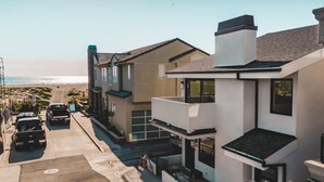A modern two-story house with a balcony, a driveway, and a view of the beach.