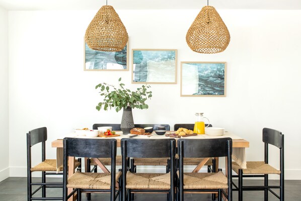 A dining area with a wooden table, black chairs, and woven pendant lights.