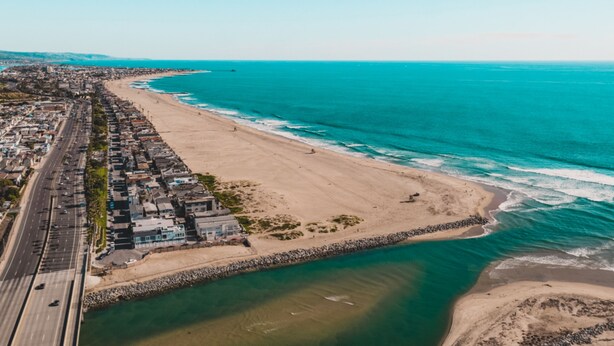 An aerial view of a coastal city with a beach, a road, and a body of water.