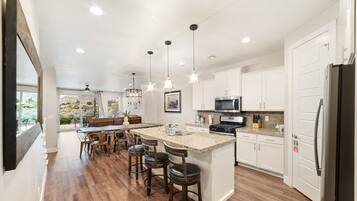 A modern kitchen with a central island, bar stools, pendant lighting, and a view to the outdoors.