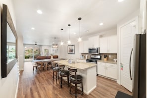 A modern kitchen with a central island, bar stools, pendant lighting, and a view to the outdoors.