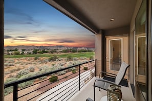 A balcony with a view of a desert landscape at sunset, a chair, and a door to the right.