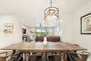 A dining area with a wooden table, metal chairs, a hanging light fixture, and a view of a living room with a brown sofa and a vase. - Sleeps 16 w/ 4 Kings - Bunk Loft on the 18th Hole (St. George)