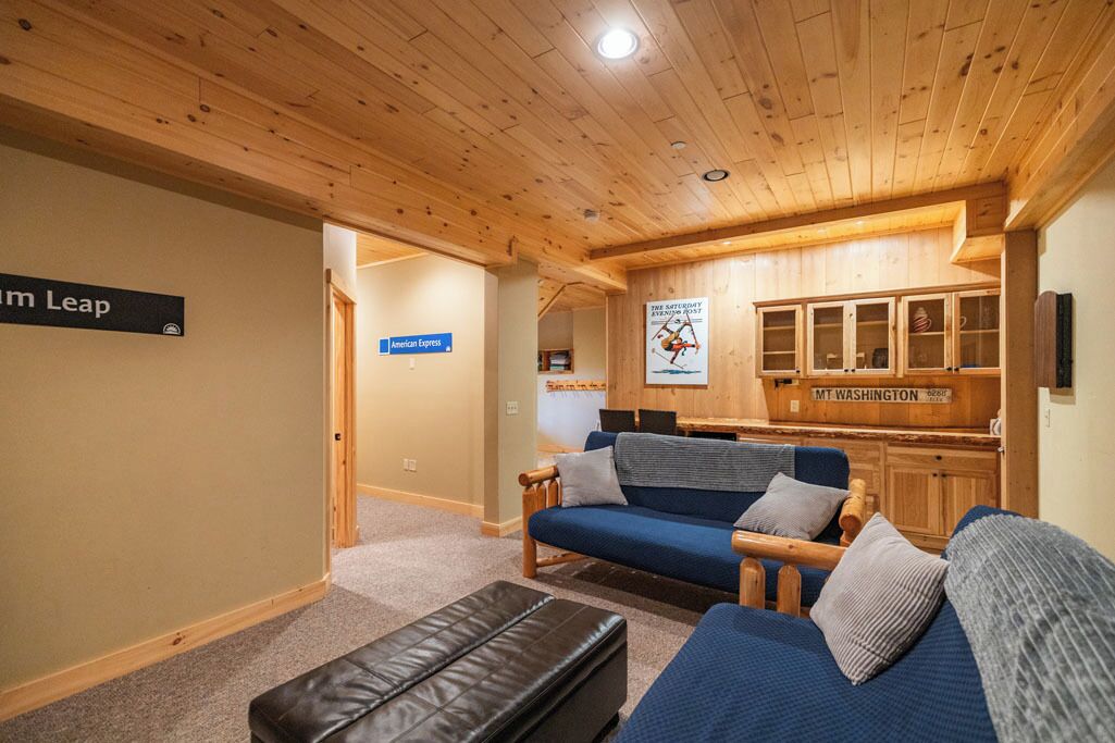 A cozy room with a blue sofa, a leather ottoman, and wooden cabinets. There is a sign for 'American Express' and a sign for 'Mt. Washington'.