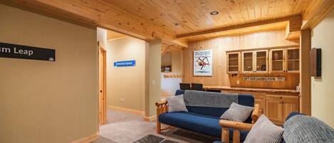 A cozy room with a blue sofa, a leather ottoman, and wooden cabinets. There is a sign for 'American Express' and a sign for 'Mt. Washington'.