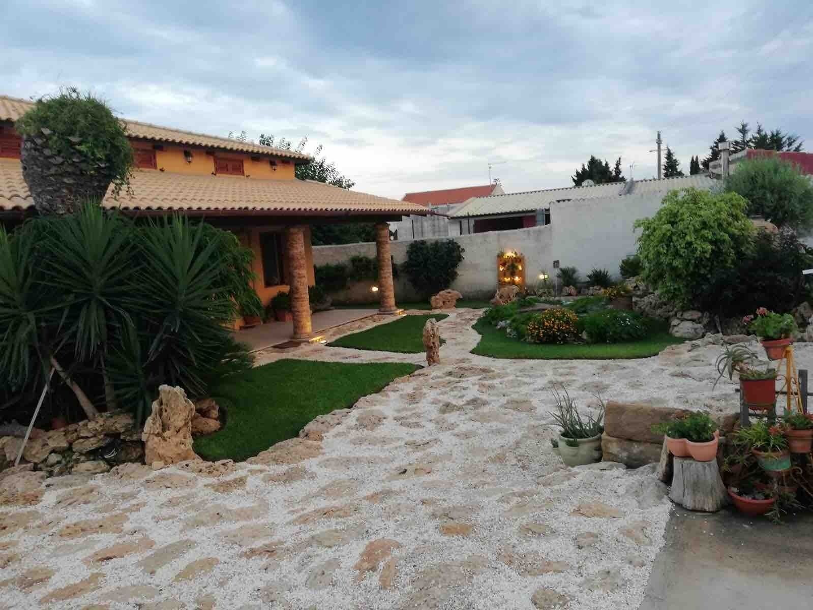 Un patio con sendero de piedra, palmeras y plantas en macetas.