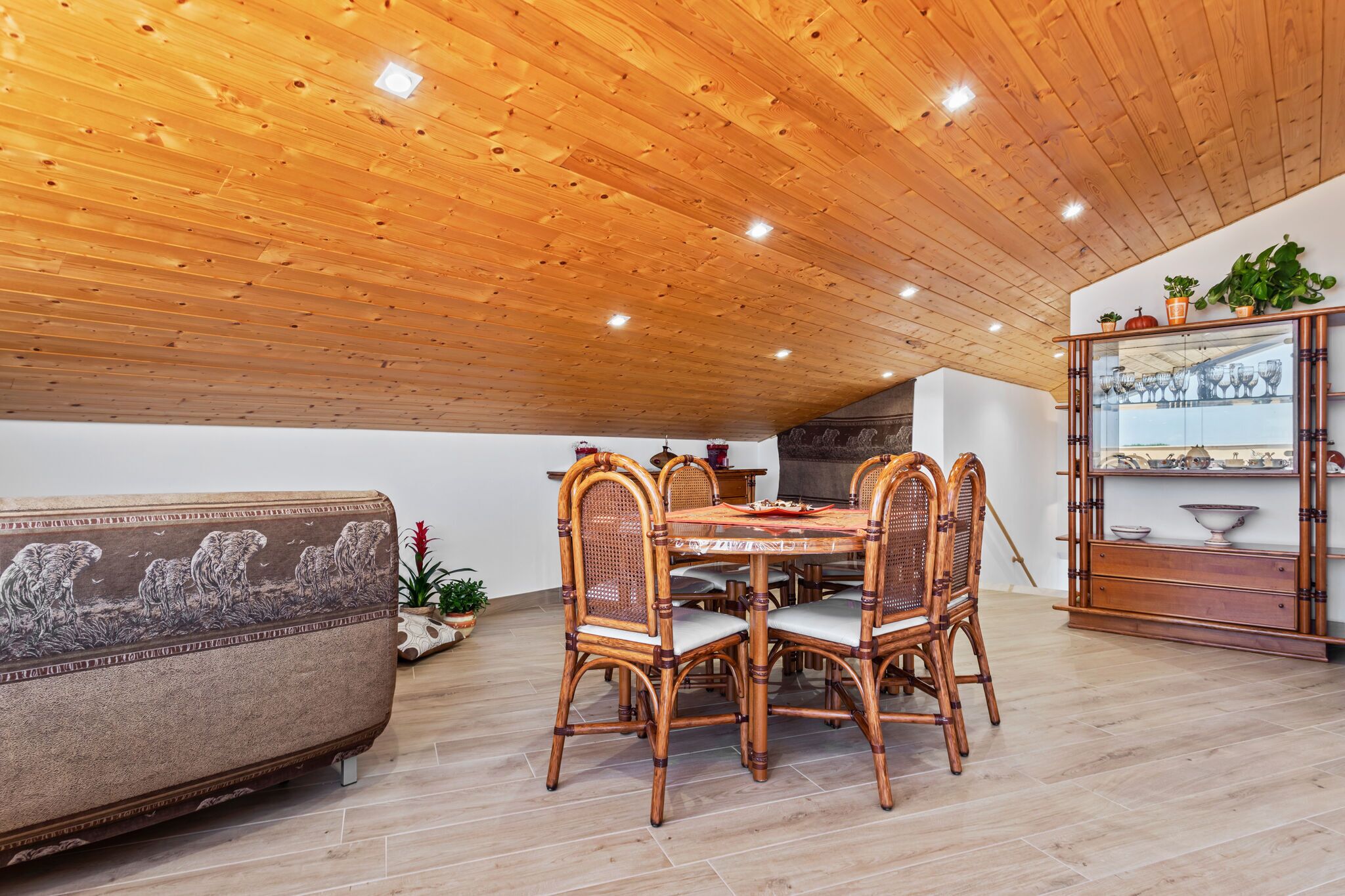 Un espace repas avec un plafond en bois, une table ronde et des chaises en osier.