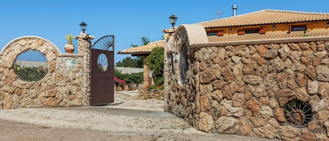 A stone-walled building with a traditional tiled roof, a metal gate, and a clear blue sky.