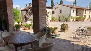 A patio area with a round table and chairs, surrounded by potted plants and a view of a building with a tiled roof. - Relaxing historic villa,  cycle path to the city center, lake, Valpolicella  (Corno Alto)