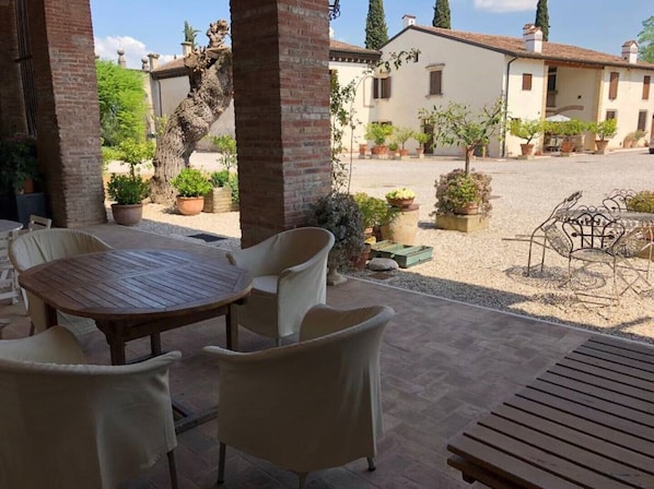 A patio area with a round table and chairs, surrounded by potted plants and a view of a building with a tiled roof.