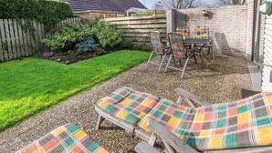 A patio with two lounge chairs and a table, surrounded by a gravel area and a wooden fence.