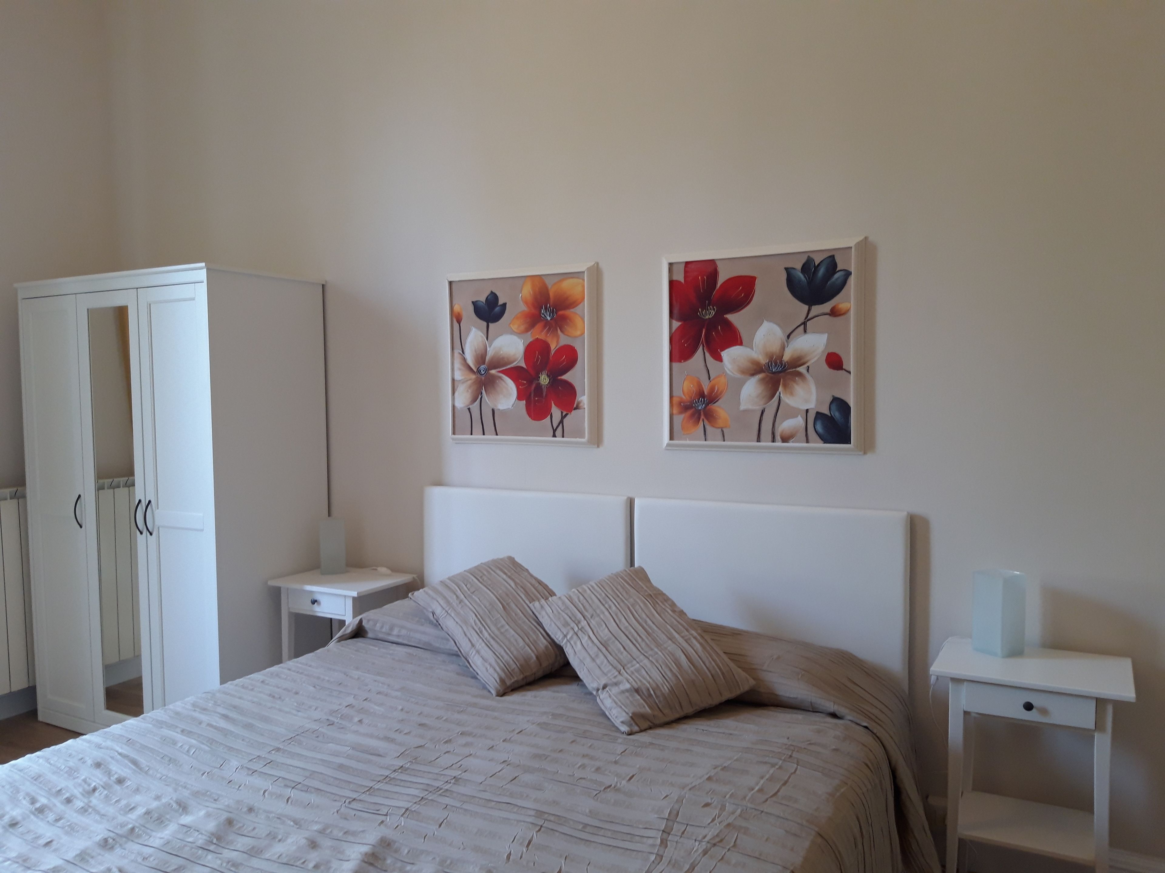 A bedroom with a bed, two nightstands, a wardrobe, and two floral wall art pieces.