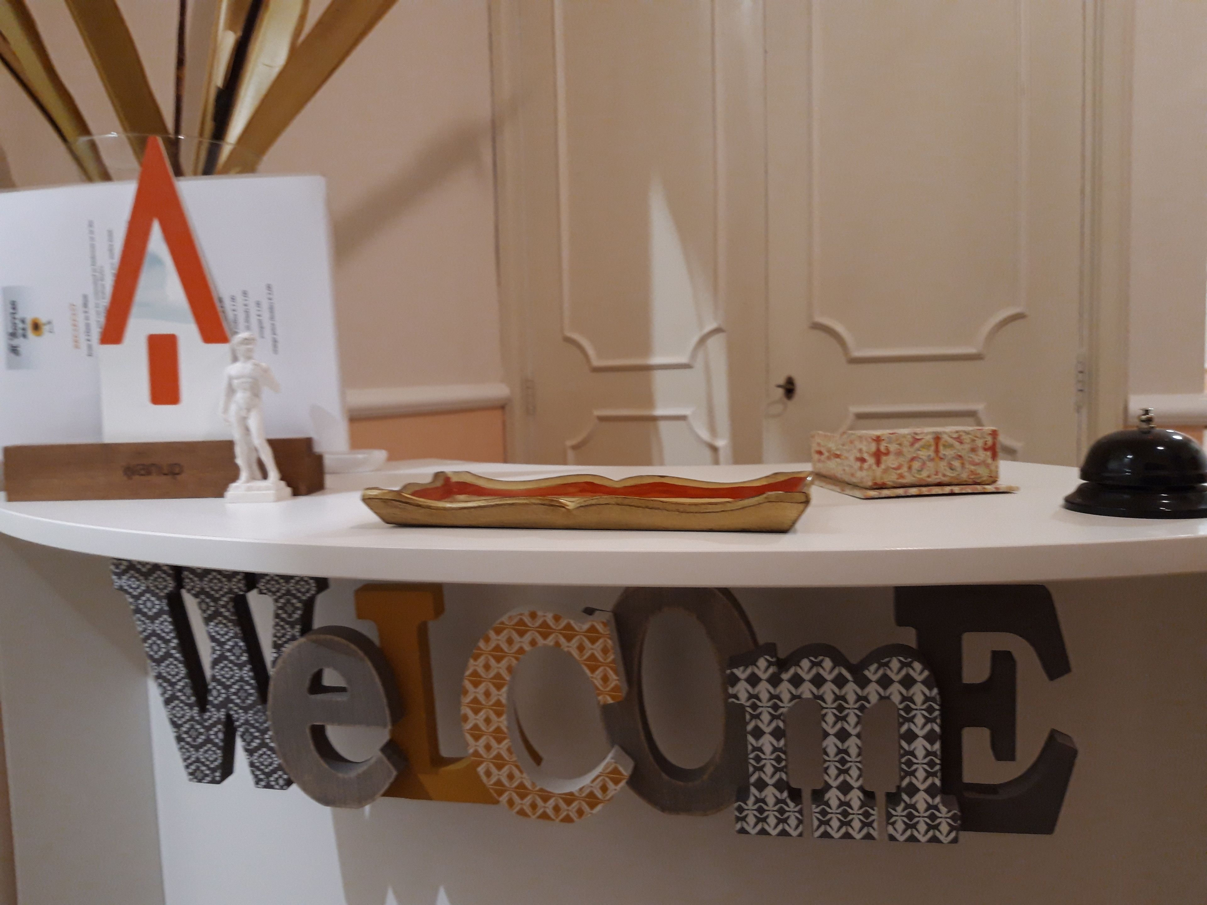 A reception desk with a 'Welcome' sign, a statue, a tray, and a patterned box.