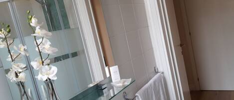 A bathroom with a glass-topped vanity, white orchid flowers, a large mirror, and a white towel hanging on a rack.