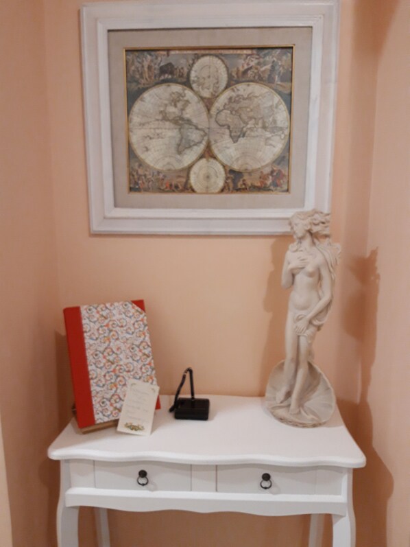 A white console table with a framed artwork above it, a red book, a small black bag, and a white statue. - Il Sorriso (Florence)