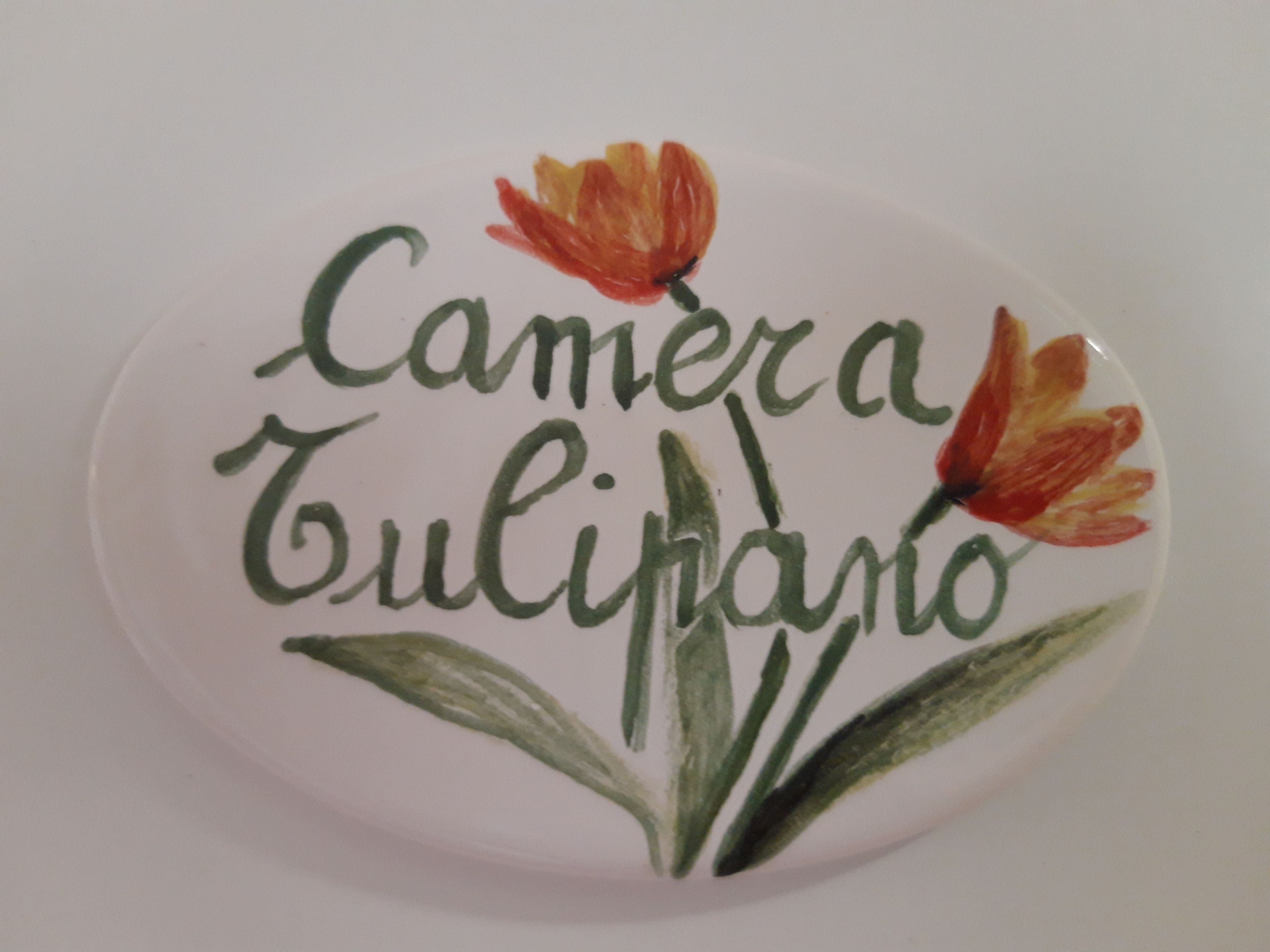 A round, white plaque with the name "Camera Tulipario" and two stylized tulip flowers.