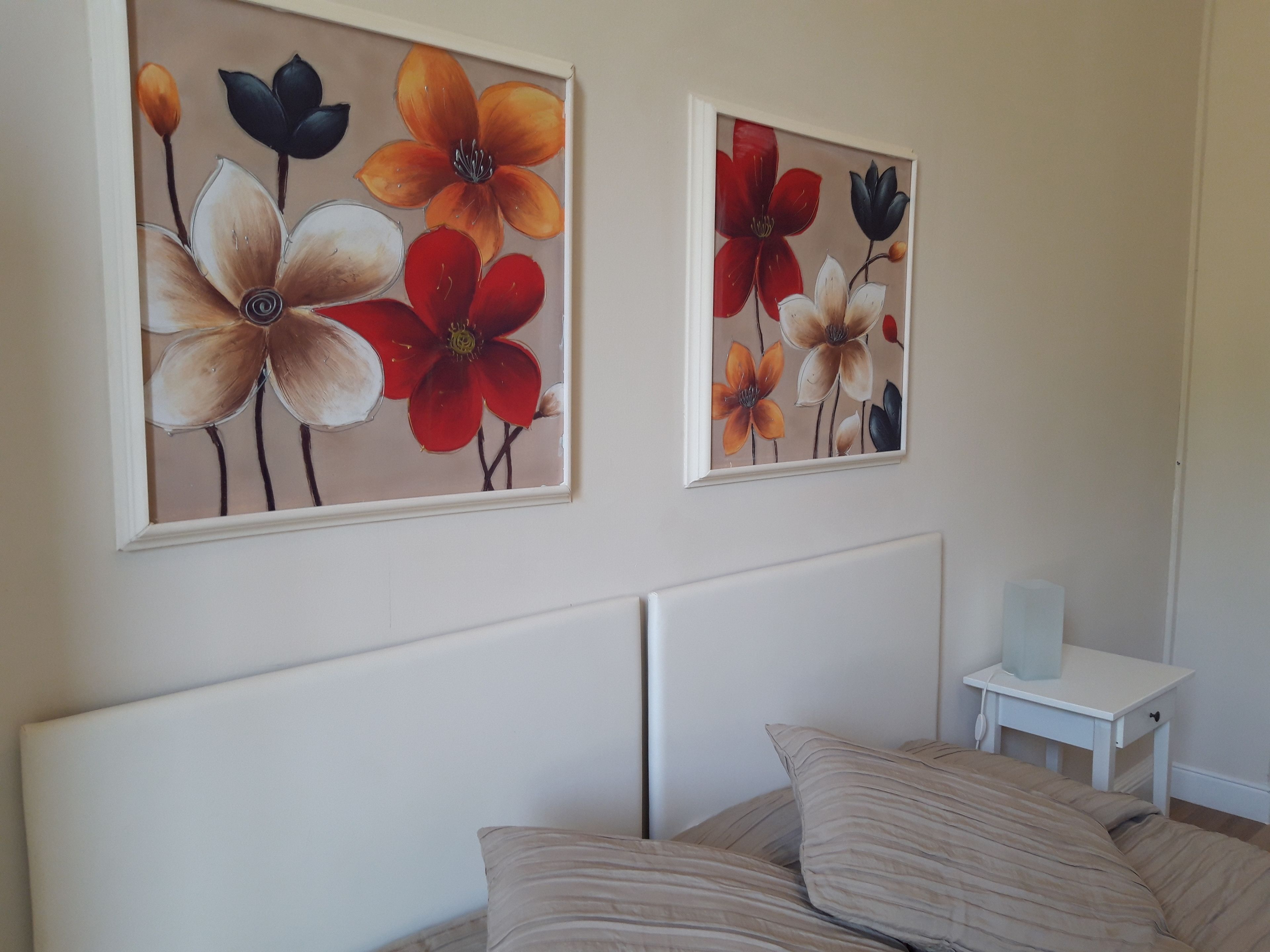A bedroom with a bed, a nightstand, and two wall-mounted paintings of flowers.