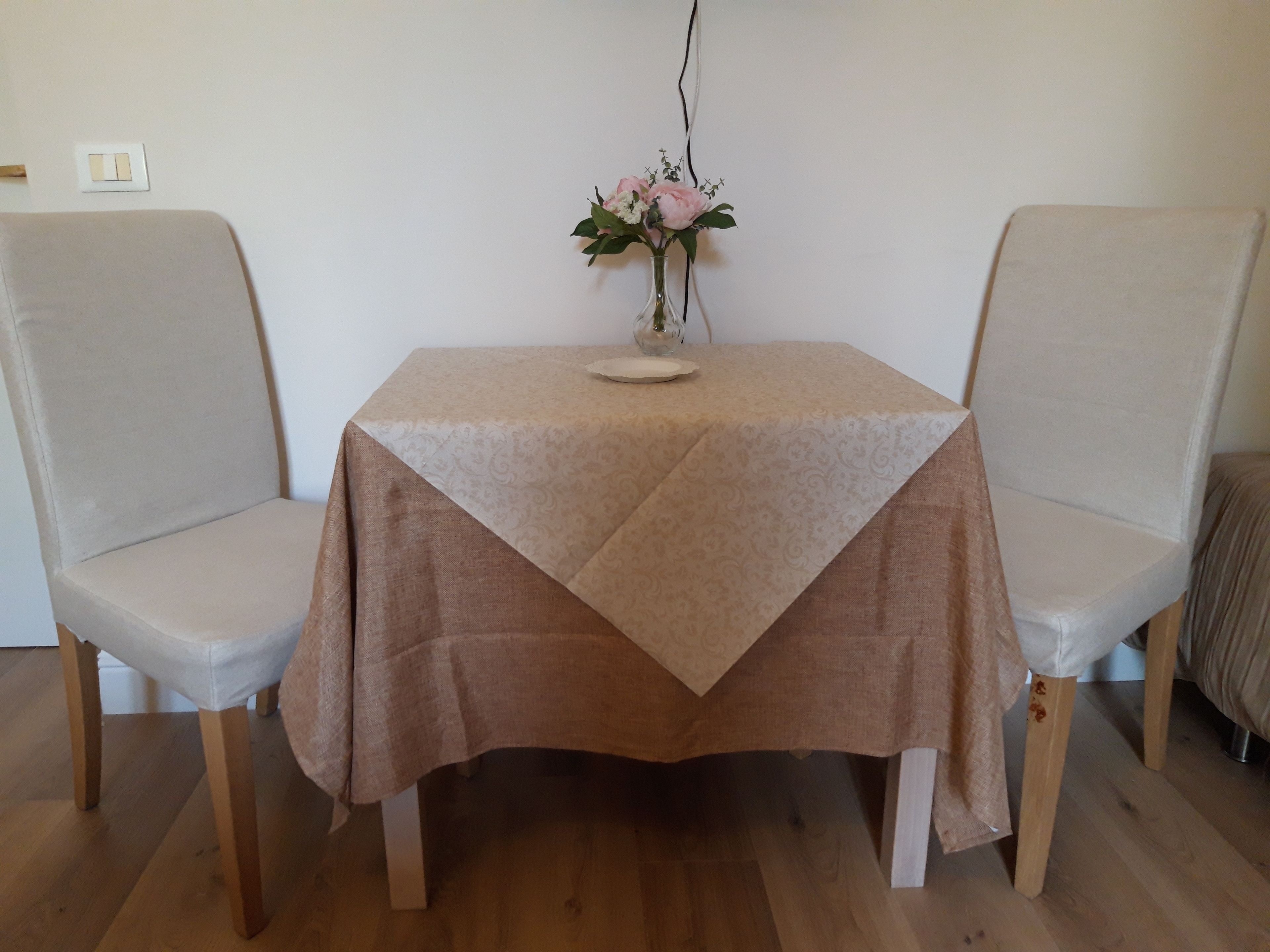 A dining table with a brown tablecloth, two chairs, and a vase with flowers on the table.