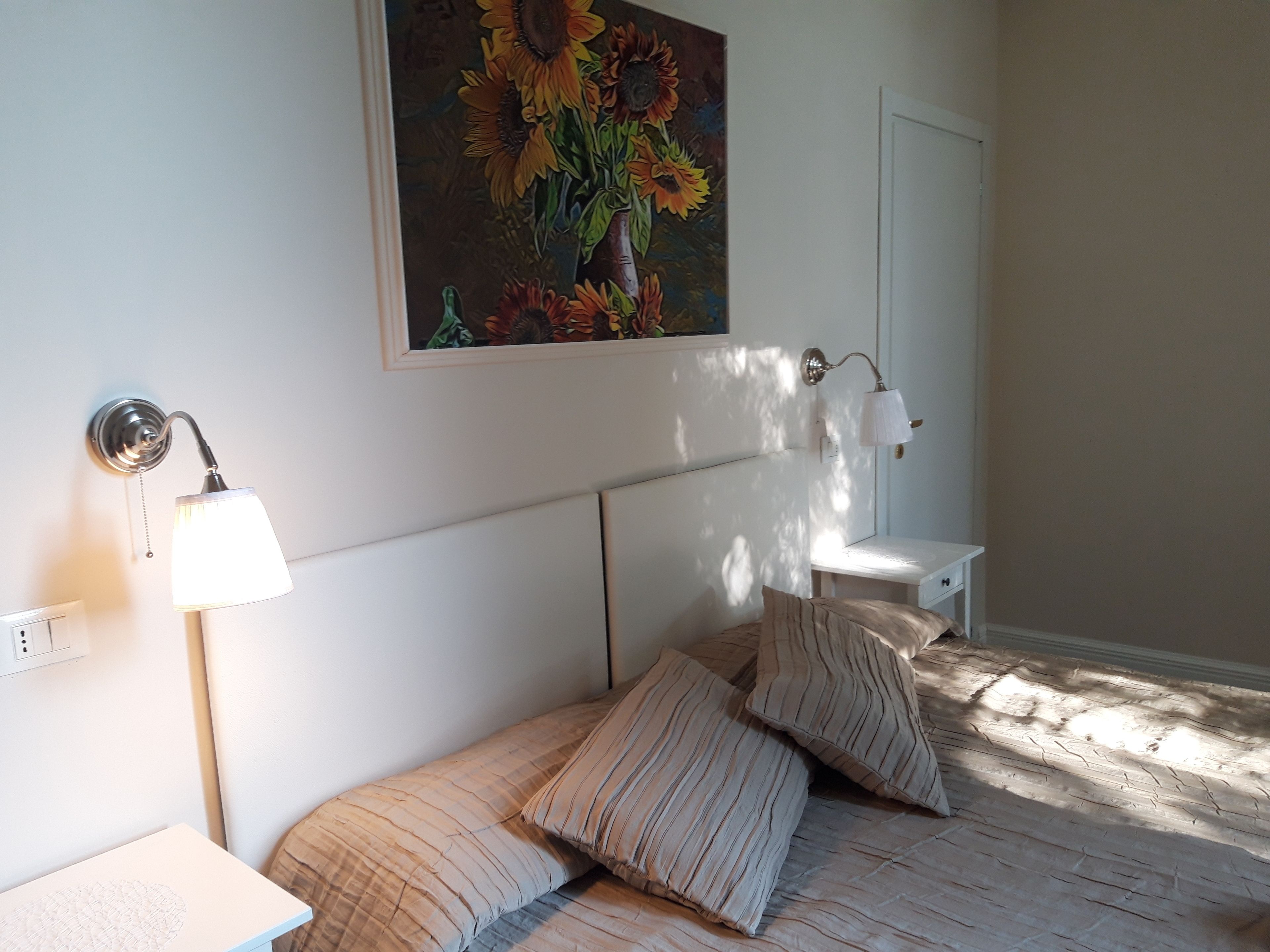 Un dormitorio con cama, mesita de noche, lámpara de pared y un cuadro de girasoles.