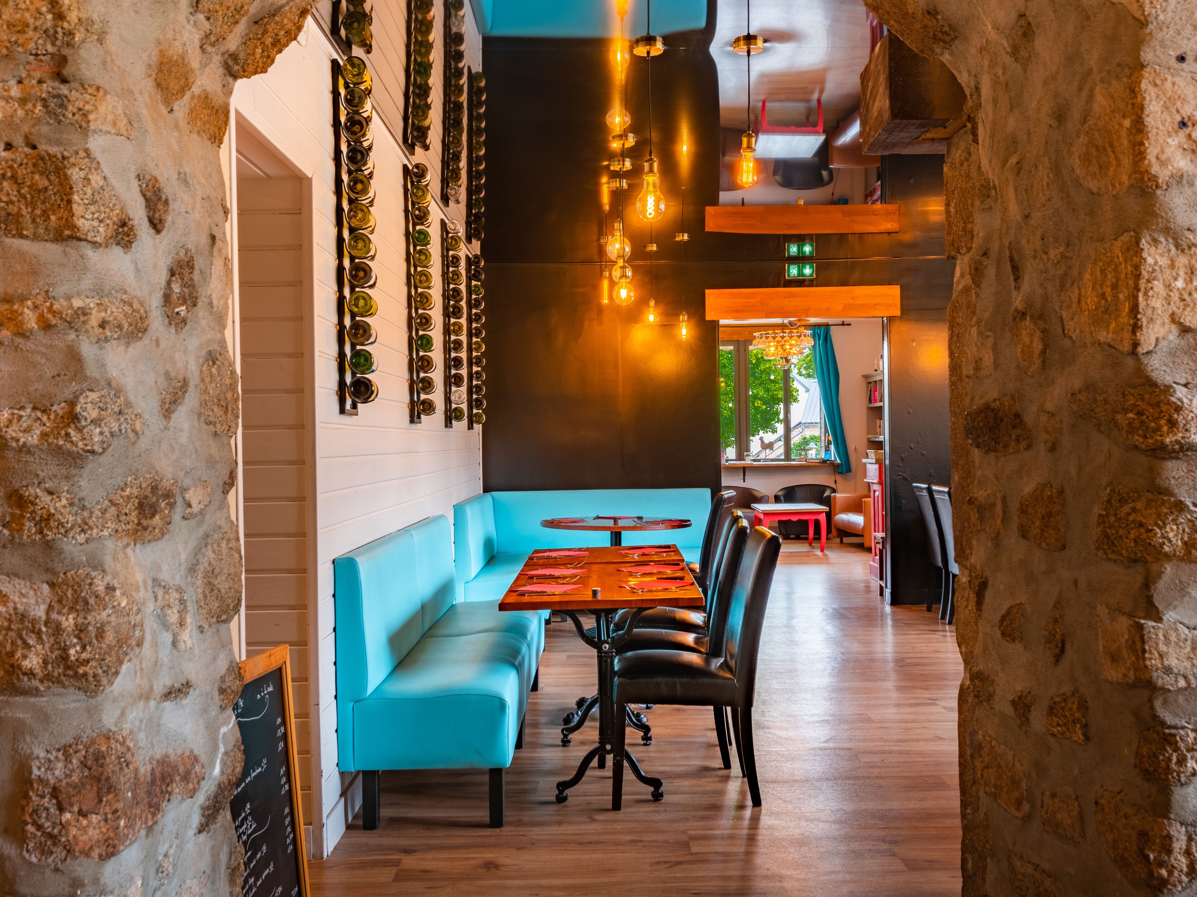 Un restaurante con pared de piedra, asientos azules, mesas de madera y luces colgantes.