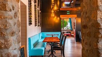 Un restaurante con pared de piedra, asientos azules, mesas de madera y luces colgantes.