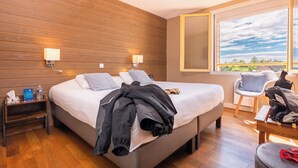 A hotel room with a large bed, wooden panel walls, a nightstand with a lamp, a chair, and a view of the outdoors. - Le Relais des Lacs (Planchez)