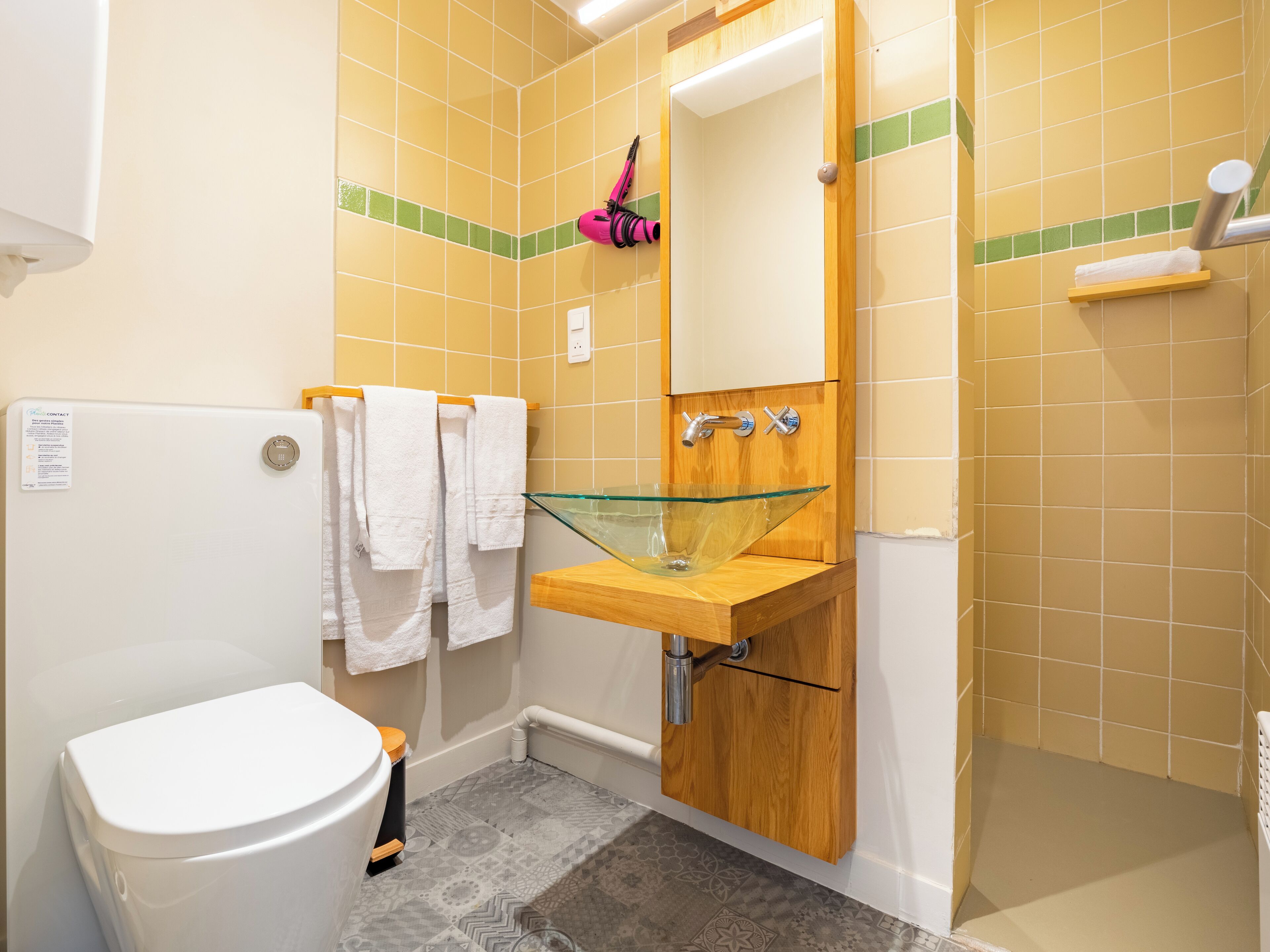 Un baño con un inodoro blanco, un lavabo de vidrio y un mueble de tocador de madera.