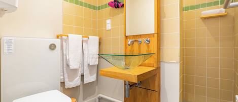 Un baño con un inodoro blanco, un lavabo de vidrio y un mueble de tocador de madera.