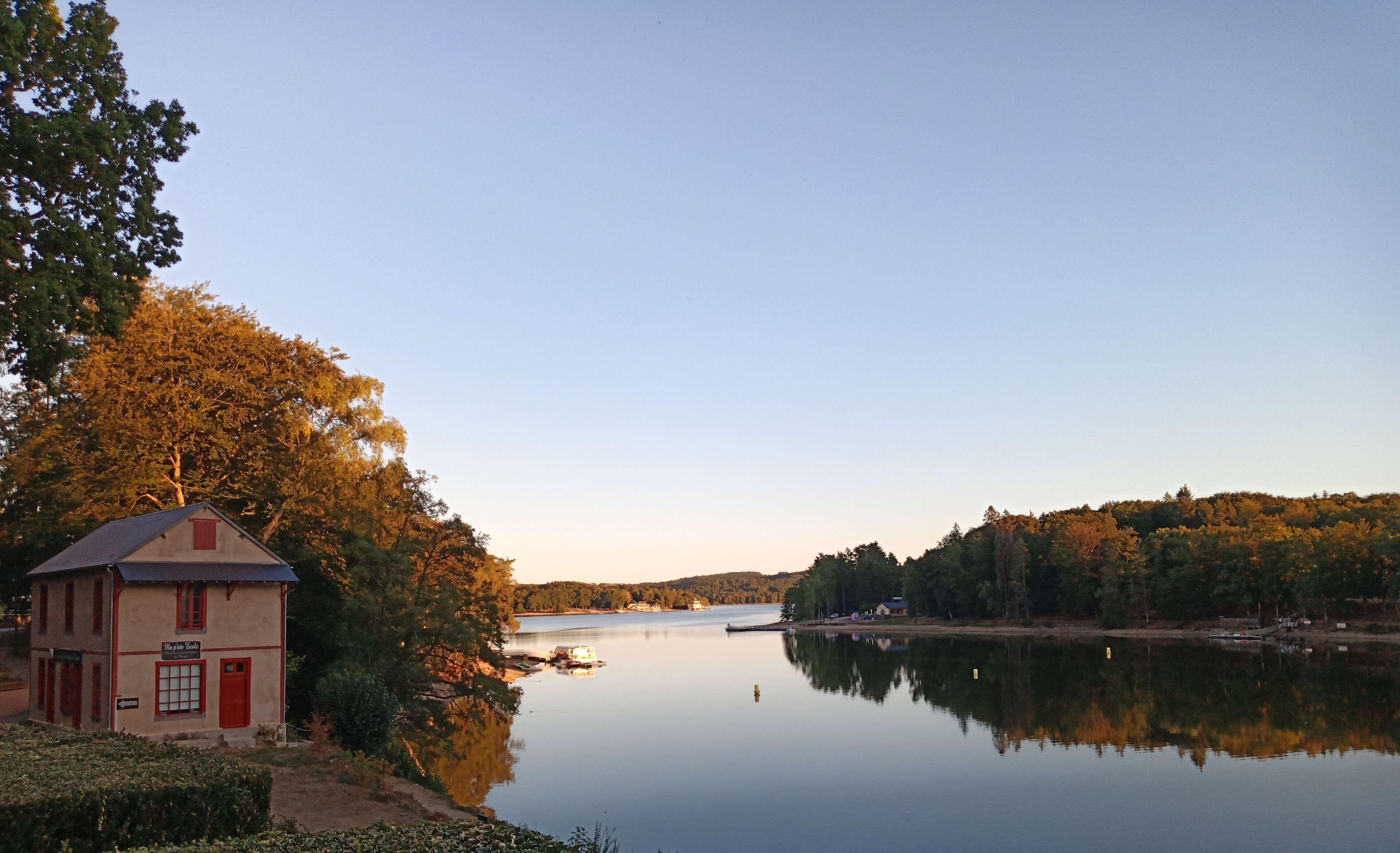 Un edificio sul lago con una porta rossa e finestre, circondato da alberi e un lago tranquillo.
