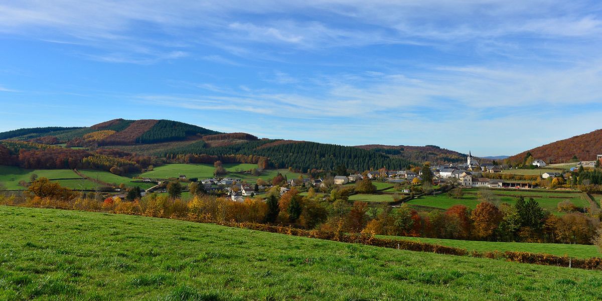 A rural landscape with a village, green fields, and hills in the background.