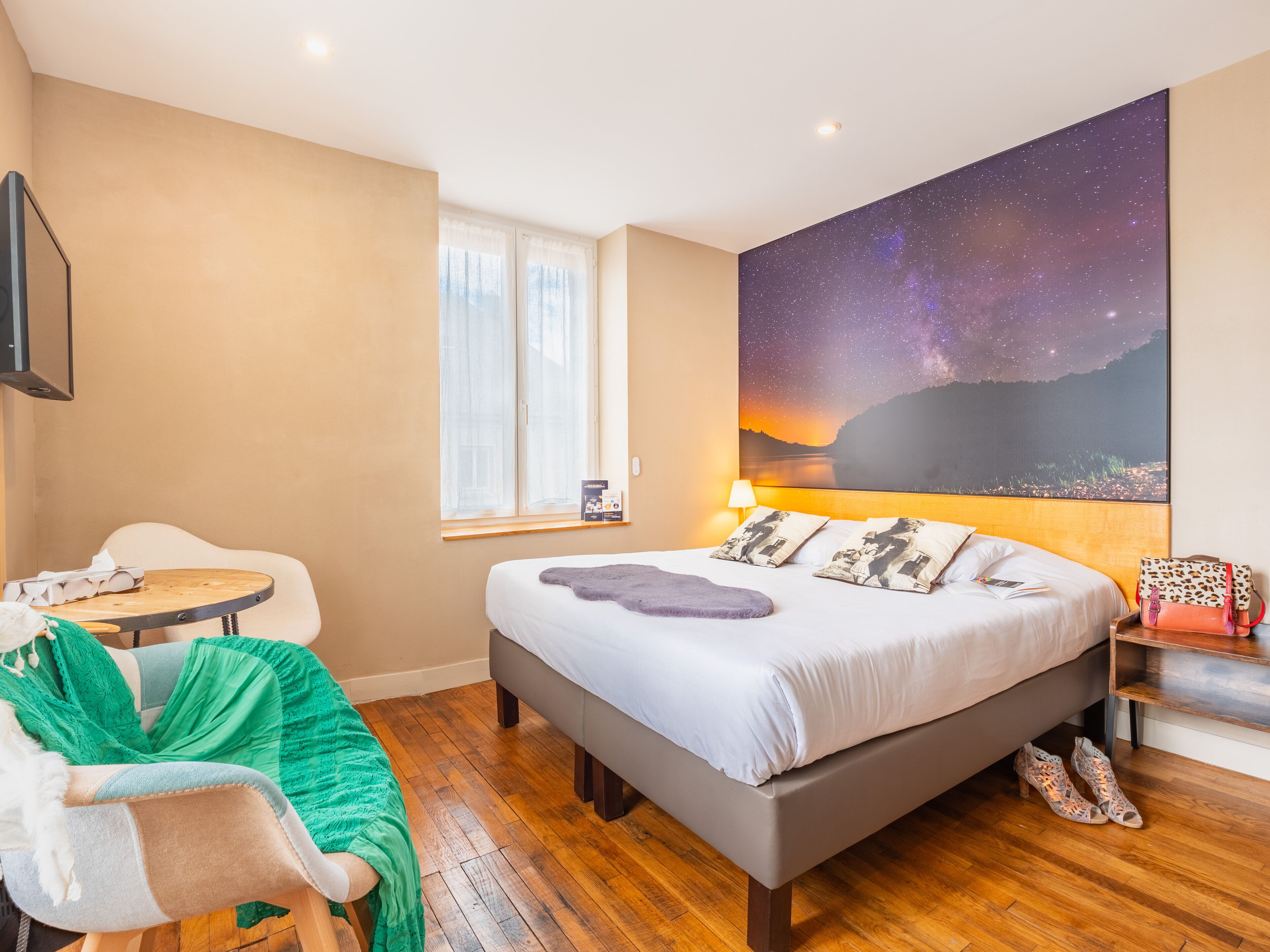 Une chambre à coucher comprenant un lit, une chaise, une table, une table de chevet, une lampe et un grand tableau représentant un ciel étoilé.