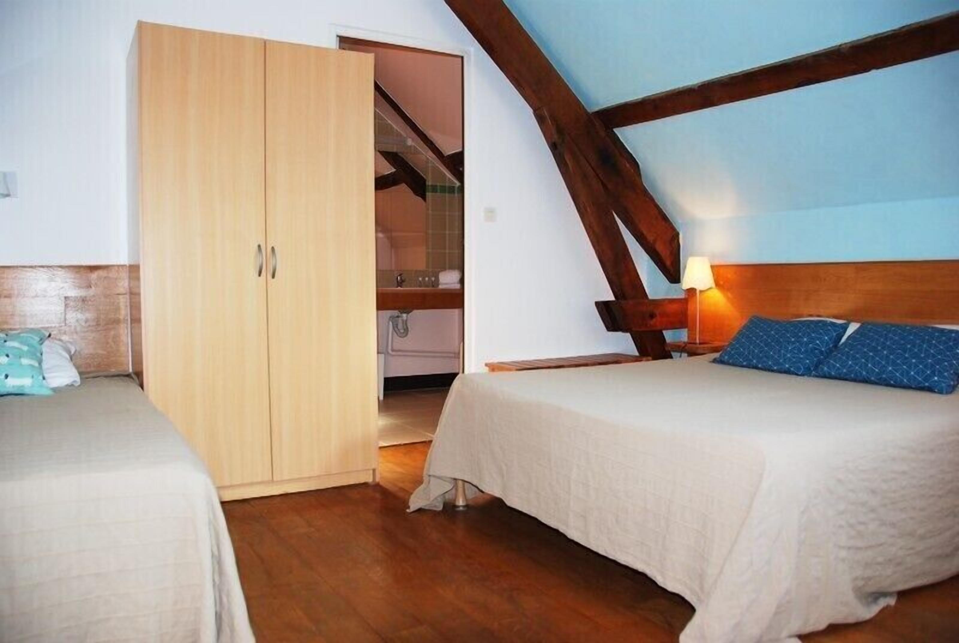 A bedroom with a wooden wardrobe, a bed with a headboard, and a nightstand with a lamp.