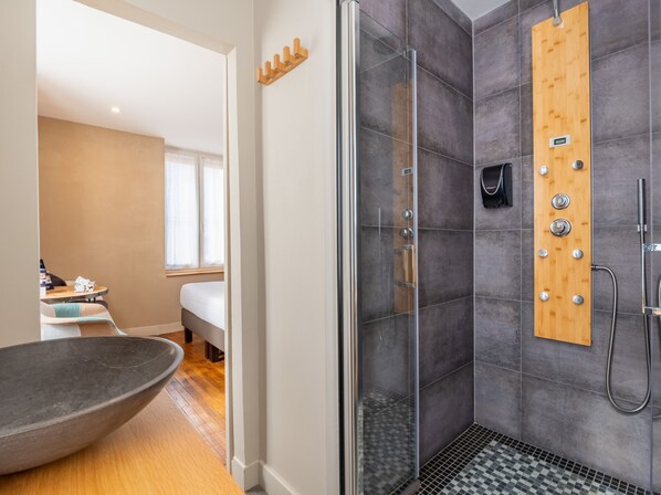 Un baño moderno con ducha de vidrio, panel de madera con toallero y un lavabo grande tipo cuenco.
