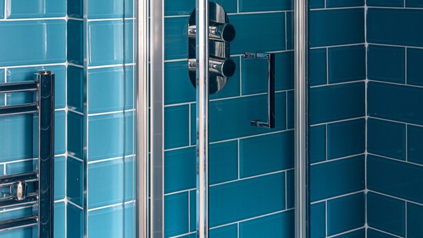 Une salle de bain avec des murs recouverts de carreaux bleus et une douche à parois de verre.