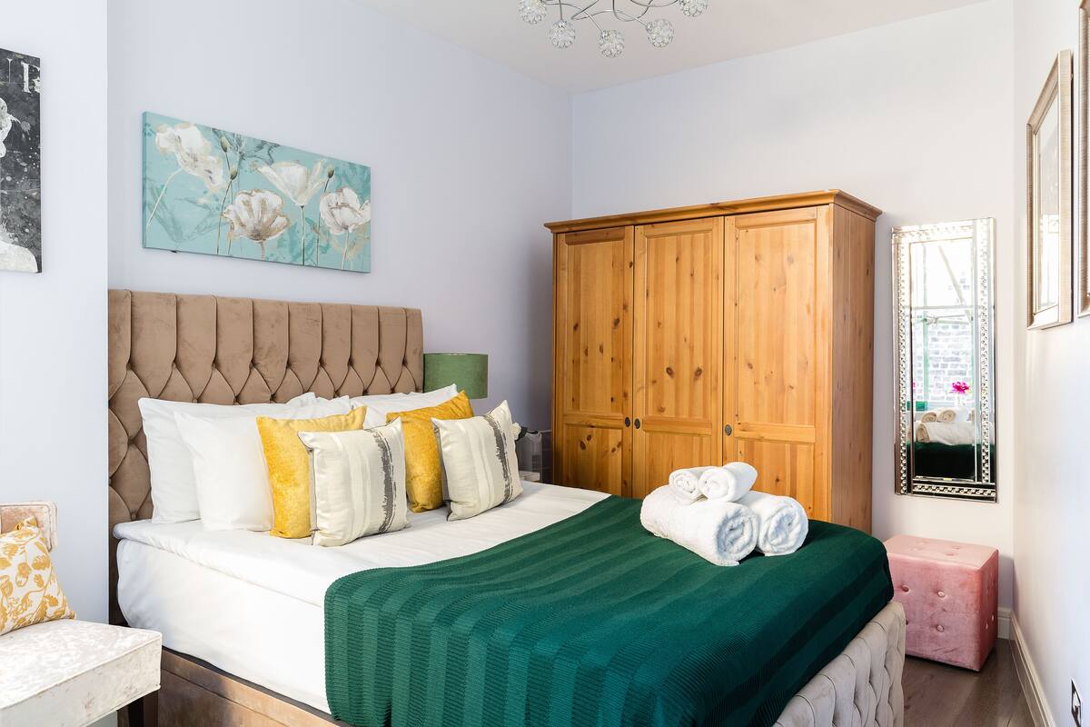 Une chambre à coucher avec un lit, une armoire en bois, une couverture verte et un tableau accroché au mur.