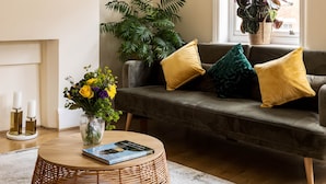Un salon comprenant un canapé, une table basse ronde, une horloge et une fenêtre donnant sur des immeubles.