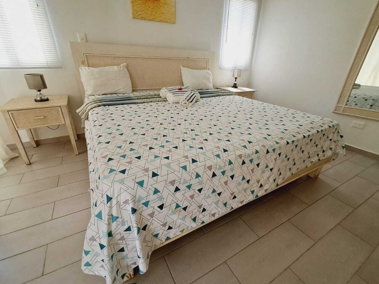 Une chambre à coucher avec un lit, une table de chevet, une lampe et une fenêtre.