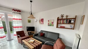 A modern living room with a grey sofa, red armchairs, a wooden coffee table, and a TV on a wooden stand. - Holiday house starfish, only 2km to the North Sea, very child-friendly  (Hamswehrum)