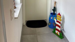 A narrow hallway with a white door, a black doormat, a small shelf with a striped umbrella, and a colorful painting of a lighthouse. - Holiday house starfish, only 2km to the North Sea, very child-friendly  (Hamswehrum)