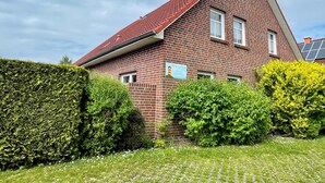 A red brick house with a sloped roof, a sign indicating a 'Verwaltetes Ferienhaus', and a hedge in the foreground. - Holiday house starfish, only 2km to the North Sea, very child-friendly  (Hamswehrum)