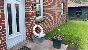 A brick house with a white door, a window with a bell, and a garden with a flower pot. - Holiday house starfish, only 2km to the North Sea, very child-friendly  (Hamswehrum)