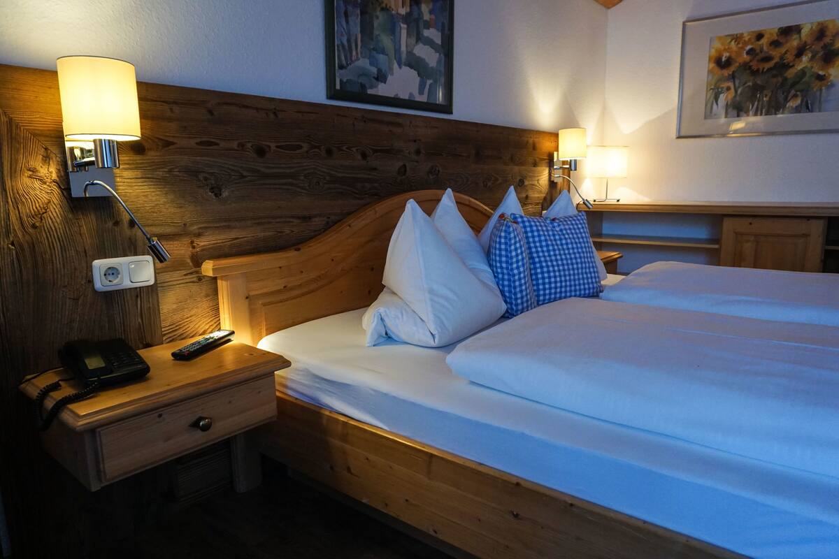 Ein Hotelzimmer mit einem hölzernen Kopfteil, einem Nachttisch mit Lampe, einem Telefon und einem karierten Kissen.