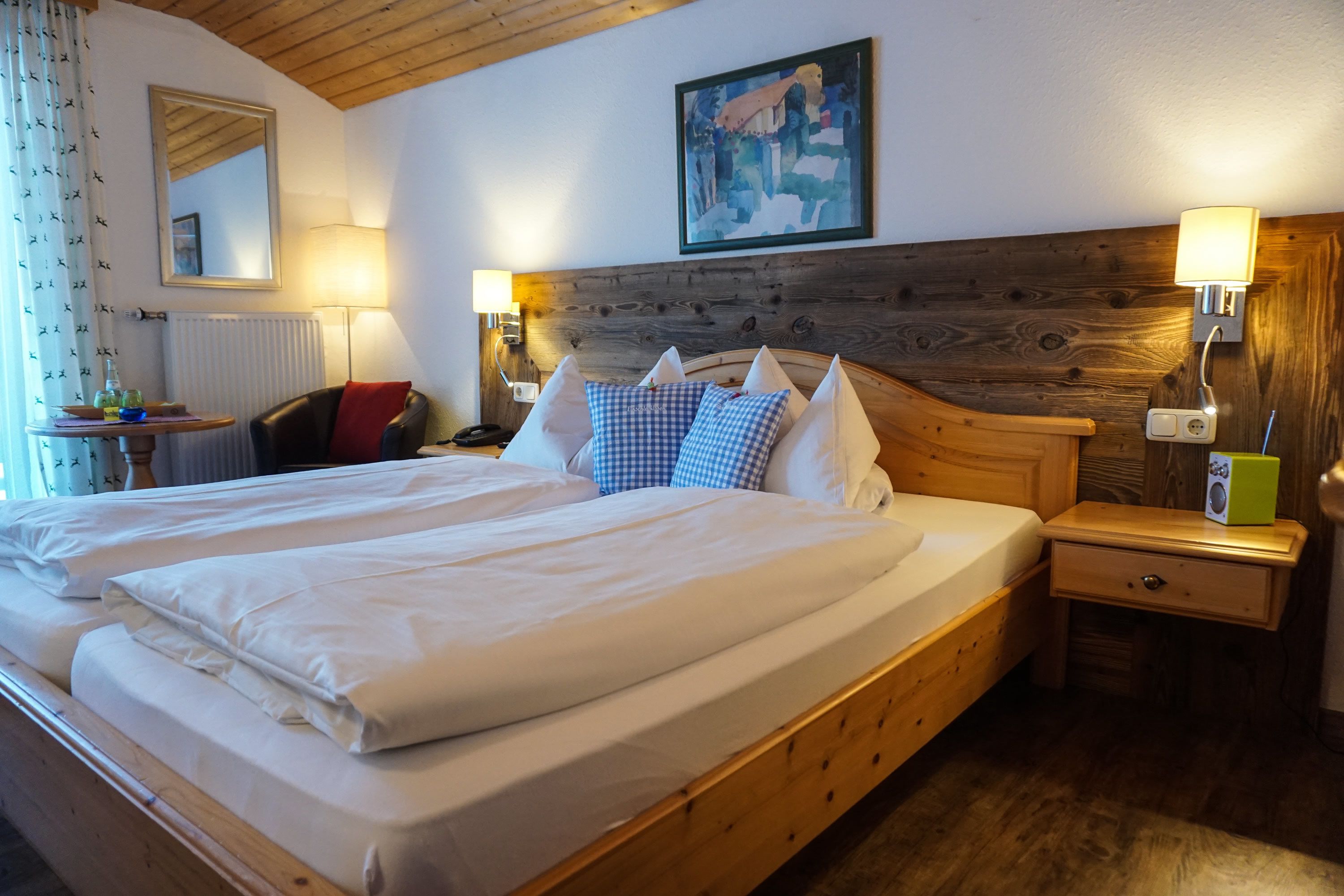 A double bed with white linens, a wooden headboard, bedside lamps, a nightstand, and a painting on the wall.