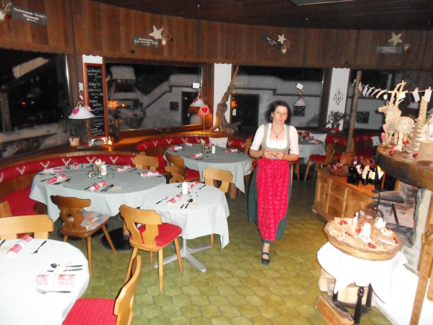 A restaurant with round tables, wooden chairs, and a woman walking through the dining area.
