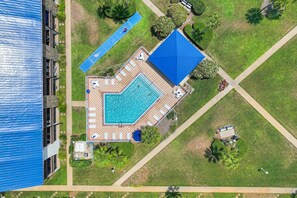 Luftaufnahme eines Hotels mit Schwimmbad, Liegestühlen und einem Tennisplatz.