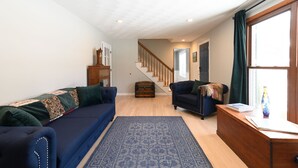 A living room with a blue sofa, a wooden chest, and a staircase leading to another room. - .6 Walk to Carmel Midtown. Quiet and secure neighborhood. Plus massage chair! (Carmel)